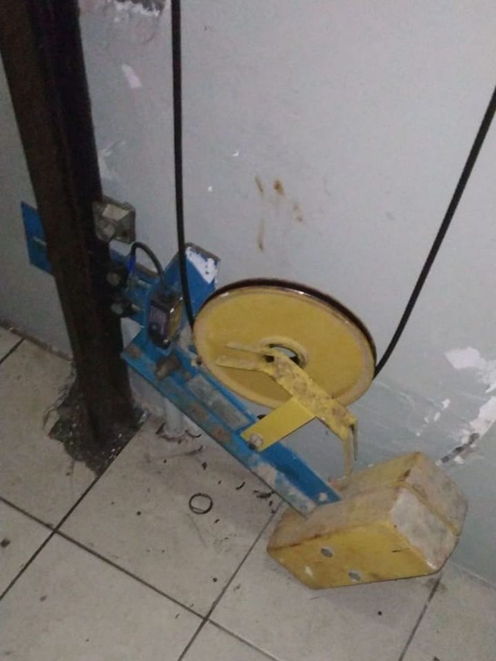 На этом рисунке показано устройство, установленное на стене. Устройство состоит из желтого блока, установленного на синей раме. В нижней части блока также виден желтый блок. Рядом с устройством подсоединено несколько проводов, а пол вокруг него выложен керамической плиткой, которая выглядит чистой, хотя на ней есть небольшие загрязнения. Стена за прибором выглядит несколько потрескавшейся и грязной, что просто указывает на окружающую среду.