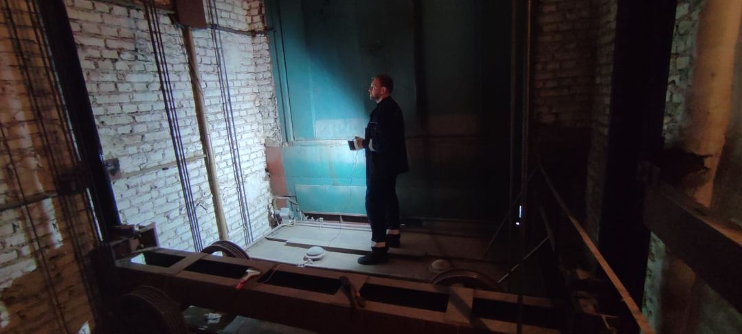 На этом снимке четверо мужчин стоят бок о бок. Кажется, что они позируют в помещении, которое может иметь промышленное или техническое назначение. Фон состоит из машины синего цвета с несколькими панелями, указывающими направление. Мужчины были одеты в повседневную одежду; на одном из них была синяя футболка, в то время как на другом были куртка и брюки разных цветов. Все улыбались и казались знакомыми друг другу. В комнате довольно хорошее освещение, что свидетельствует о приятной атмосфере.