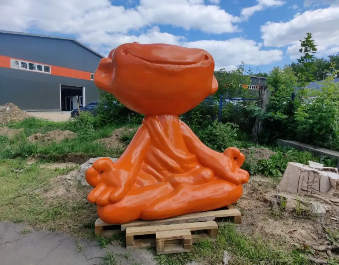 Огромный оранжевый пельмень в позе лотоса на фоне завода